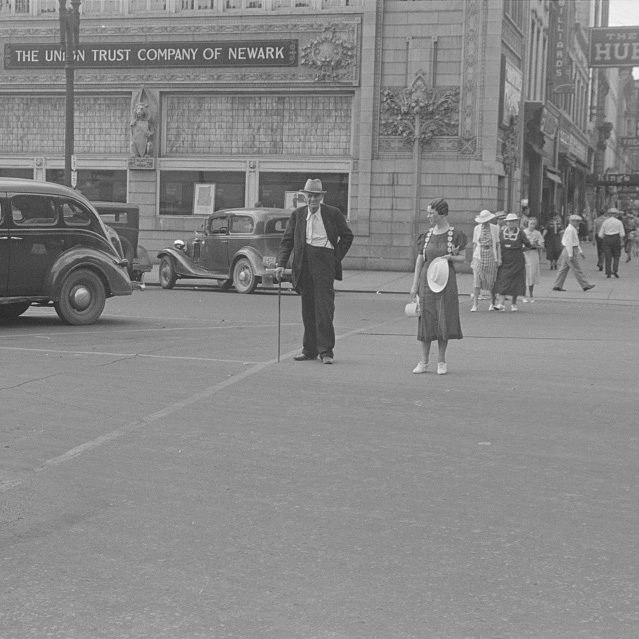 Image of 1940s car and people walking across a street in front of the Sullivan Building in downtown Newark, Ohio