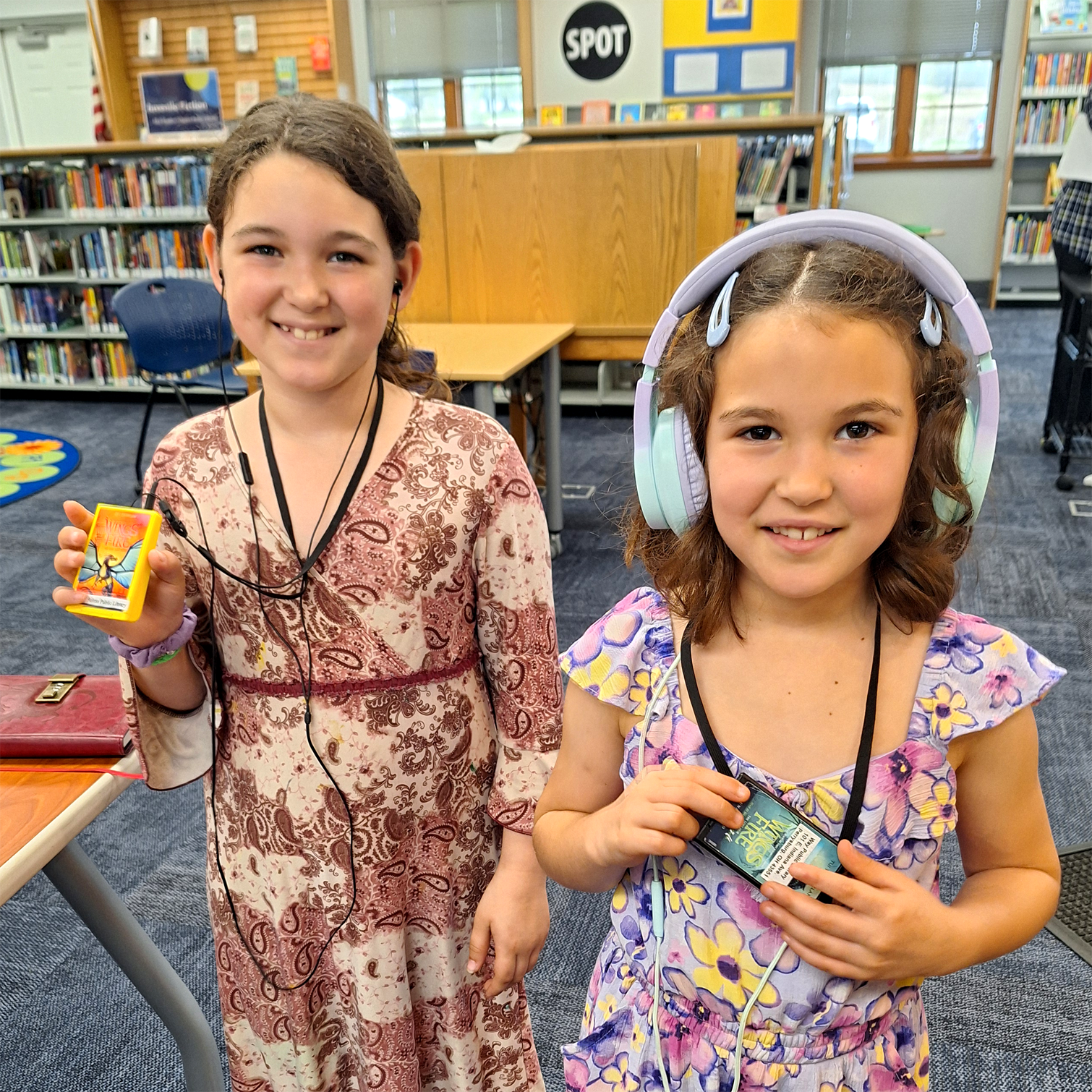Two girls smiling with Playaways in library